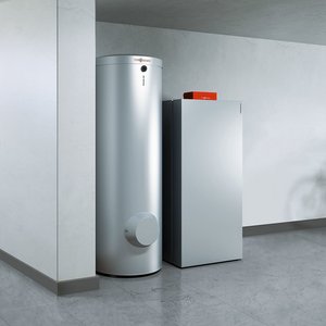 In einem minimalistischen Raum stehen ein schlanker Kühlschrank und ein hoher Warmwasserbereiter nebeneinander an einer Wand.