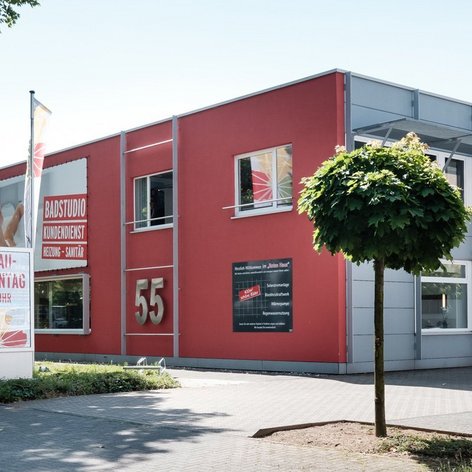 Ein modernes Gebäude mit roter Fassade und großen Fenstern, umgeben von Bäumen und einem gepflegten Parkplatz.