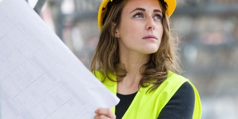 Eine Frau mit Bauhelm hält eine Zeichnung auf einer Baustelle