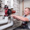 Fachmann installiert eine Wasserpumpe in einem Keller Ein Handwerker arbeitet konzentriert an einer Wasserpumpe in einem Keller, um die Installation zu überprüfen.