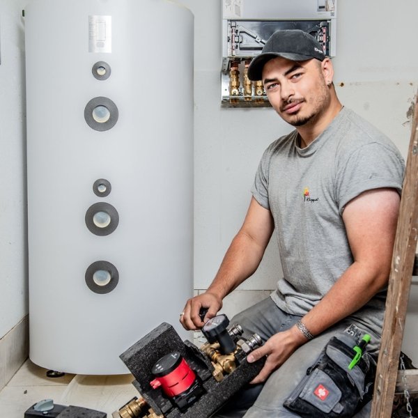 Der Techniker lächelt, während er an einer Heizungsinstallation arbeitet, umgeben von Rohren und einem großen weißen Tank.