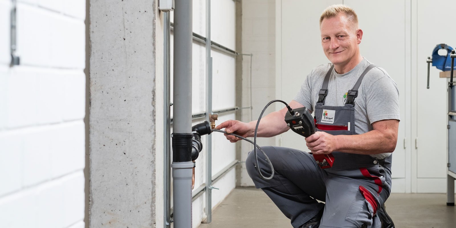 In einer hellen Werkstatt repariert ein Mann ein Rohrsystem, während er konzentriert mit einem elektrischen Gerät arbeitet.