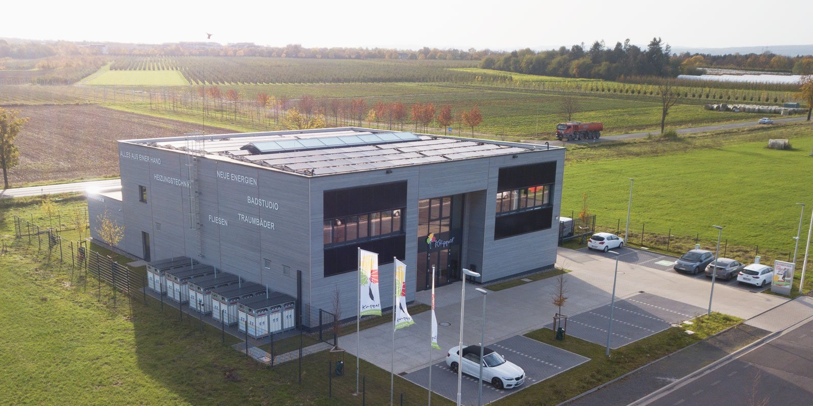 Die Fassade eines zeitgenössischen Unternehmensgebäudes, das innovative Energielösungen anbietet, vor einer ländlichen Kulisse.