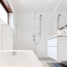 Ein modernes Badezimmer mit einer weißen Badewanne und einer eleganten Dusche, umgeben von hellen Fliesen und natürlichem Licht.