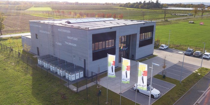 Ein modernes Gebäude mit Solarpanelen auf dem Dach, umgeben von grünen Feldern und Bäumen im Hintergrund.