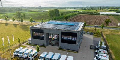 Ein modernes Gebäude mit Solarpanelen auf dem Dach, umgeben von grünen Feldern und Bäumen, strahlt Nachhaltigkeit aus.