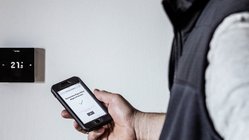 Eine Heizungssteuerung an der Wand und ein Mann der ein Handy in der Hand haelt, geoeffnet mit einer Steuerungs App