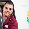 Professioneller Lieferdienst mit freundlichem Fahrer Ein lächelnder Mann mit Schnurrbart schaut aus dem Fenster eines Lieferwagens, während Regentropfen die Scheibe benetzen.