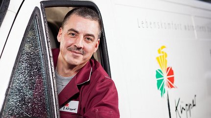 Professioneller Lieferdienst mit freundlichem Fahrer Ein lächelnder Mann mit Schnurrbart schaut aus dem Fenster eines Lieferwagens, während Regentropfen die Scheibe benetzen.