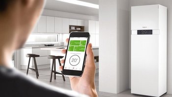Eine Person hält ein Smartphone in der Hand und steuert die Temperatur eines modernen Kühlschranks in einer hellen Küche.