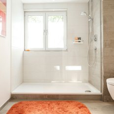 Ein modernes Badezimmer mit einer Dusche, einem weißen WC und einem orangefarbenen Teppich auf dem Boden.