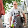 Handwerker begrüßt Kundin vor dem Haus Ein Handwerker steht an der Tür und lächelt freundlich, während er Werkzeuge in der Hand hält und bereit ist, zu helfen.