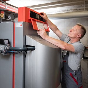 Ein Techniker überprüft die Steuerung eines Heizgeräts in einem modernen Heizungsraum, konzentriert auf die Einstellungen.