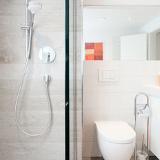 Ein modernes Badezimmer mit einer eleganten Dusche, einem weißen Waschbecken und einem großen Spiegel, der den Raum reflektiert.