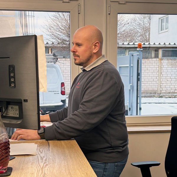 Ein Mann mit Glatze sitzt an einem Schreibtisch und arbeitet konzentriert an einem Computerbildschirm.