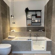 Ein modernes Badezimmer mit grauen Fliesen, einer Badewanne und einem hängenden Bademantel, der eine entspannende Atmosphäre schafft.