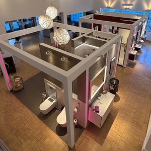 Die Ansicht eines großzügigen Ausstellungsraums mit verschiedenen Badezimmermodellen, die durch sanfte Farben und Lichtakzente hervorgehoben werden.