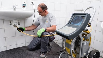 Ein Handwerker überprüft eine Abflussleitung unter einem Waschbecken mit einem speziellen Gerät zur Rohrinspektion.