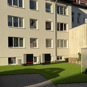 Zwei große Geräte stehen auf dem grünen Rasen vor einem mehrstöckigen Wohngebäude mit vielen Fenstern.