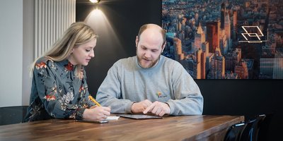 In einem modernen Raum diskutieren ein Mann und eine Frau über ein Projekt, umgeben von urbaner Kunst an der Wand.