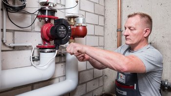 Ein Handwerker arbeitet konzentriert an einer Heizungsanlage in einem Keller, um die Pumpeninstallation zu überprüfen.