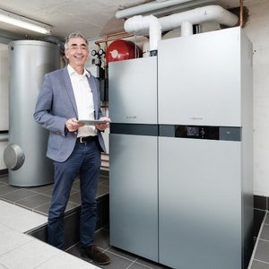 Ein lächelnder Mann steht neben einem modernen Kühlschrank und hält ein Tablet in der Hand, umgeben von technischen Geräten.