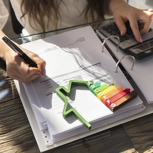 Eine Frau die an einem Ordner arbeitet auf dem ein Taschenrechner und ein Energieverbrauch zeichen liegt 