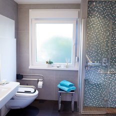 Ein modernes Badezimmer mit einer Dusche, einem Waschbecken und einer großen Fensterfront, die viel Licht hereinlässt.
