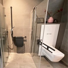 Die Dusche ist mit einem schwarzen Haltegriff ausgestattet, während das WC eine schlichte, weiße Form hat und barrierefrei ist.