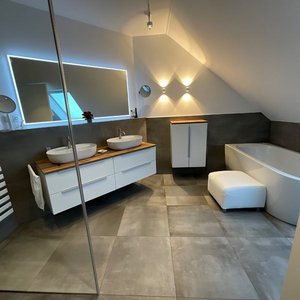 Der Raum zeigt eine stilvolle Badewanne, zwei Waschbecken und eine große Spiegelwand, alles in neutralen Farbtönen.