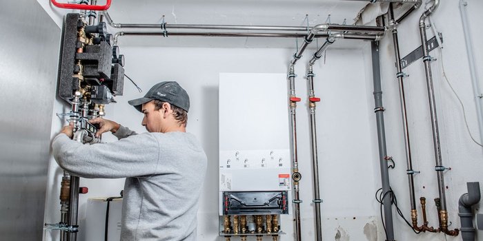 Ein Handwerker arbeitet konzentriert an einer Heizungsanlage, während er präzise Messungen an den Rohren vornimmt.