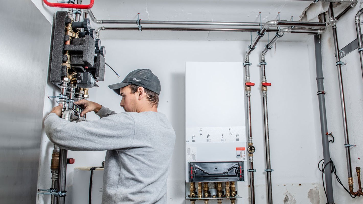 Ein Handwerker arbeitet konzentriert an einer Heizungsanlage, während er präzise Messungen an den Rohren vornimmt.