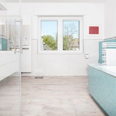 Ein modernes Badezimmer mit hellblauen Fliesen, einer Badewanne und einem großen Fenster, das Tageslicht hereinlässt.